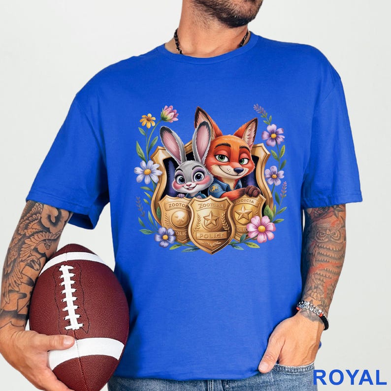 Puede incluir: Camiseta azul real con un gr&aacute;fico colorido de Judy Hopps y Nick Wilde de Zootopia, enmarcado por flores y placas de polic&iacute;a. El dise&ntilde;o incluye la palabra "POLICE" y el logotipo de Zootopia. La camiseta es de material suave.