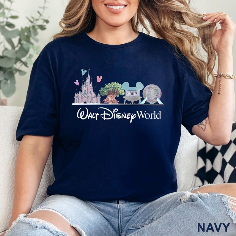 May include: Navy blue t-shirt featuring a Walt Disney World graphic. The design includes a castle, the Tree of Life, a Mickey Mouse head, and Spaceship Earth. The words "Walt Disney World" are written in white script.