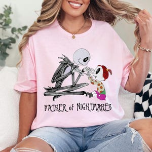 Puede incluir: Camiseta rosa claro con un dise&ntilde;o de Jack Skellington de Pesadilla antes de Navidad. La imagen muestra a Jack con un ni&ntilde;o, con el texto "FATHER of NIGHTMARES" debajo. La camiseta es de cuello redondo.