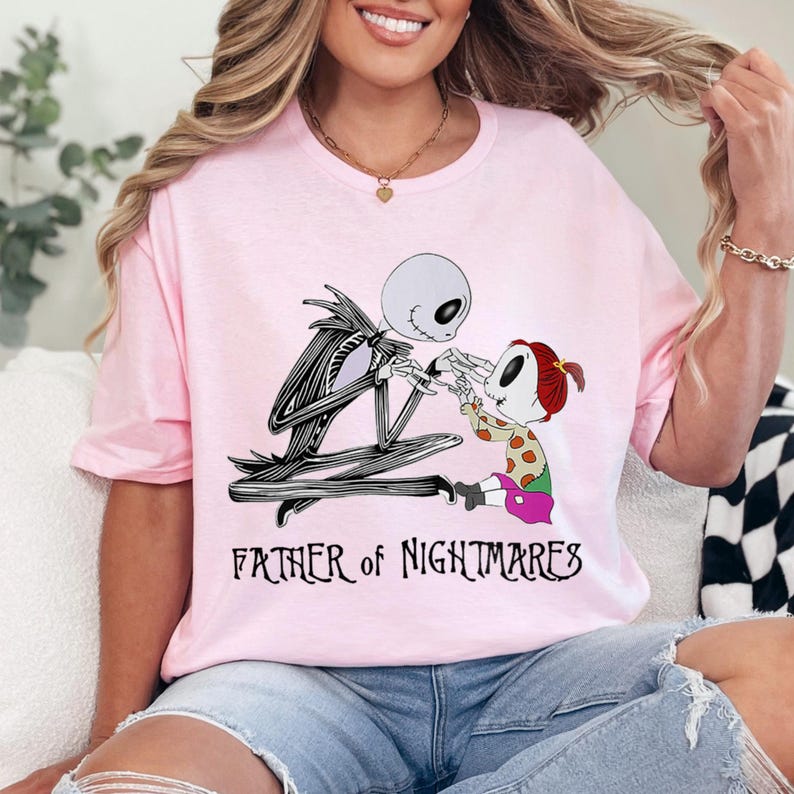 Puede incluir: Camiseta rosa claro con un dise&ntilde;o de Jack Skellington de Pesadilla antes de Navidad. La imagen muestra a Jack con un ni&ntilde;o, con el texto "FATHER of NIGHTMARES" debajo. La camiseta es de cuello redondo.
