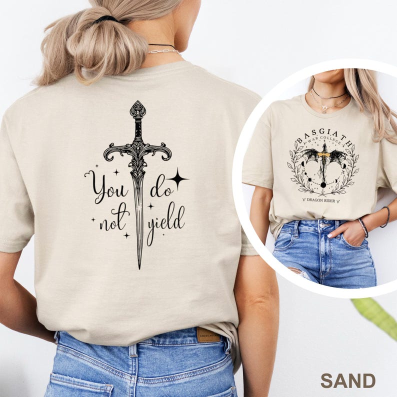 May include: Sand-colored t-shirt featuring a black sword design with the text "You do not yield." A second image shows a similar shirt with a circular design and the text "Basgiath War College Dragon Rider."