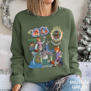 May include: Military green crewneck sweatshirt featuring a colorful graphic of characters from the animated film "Zootopia." The design includes framed portraits and the film's title. The sweatshirt is made of a soft material.