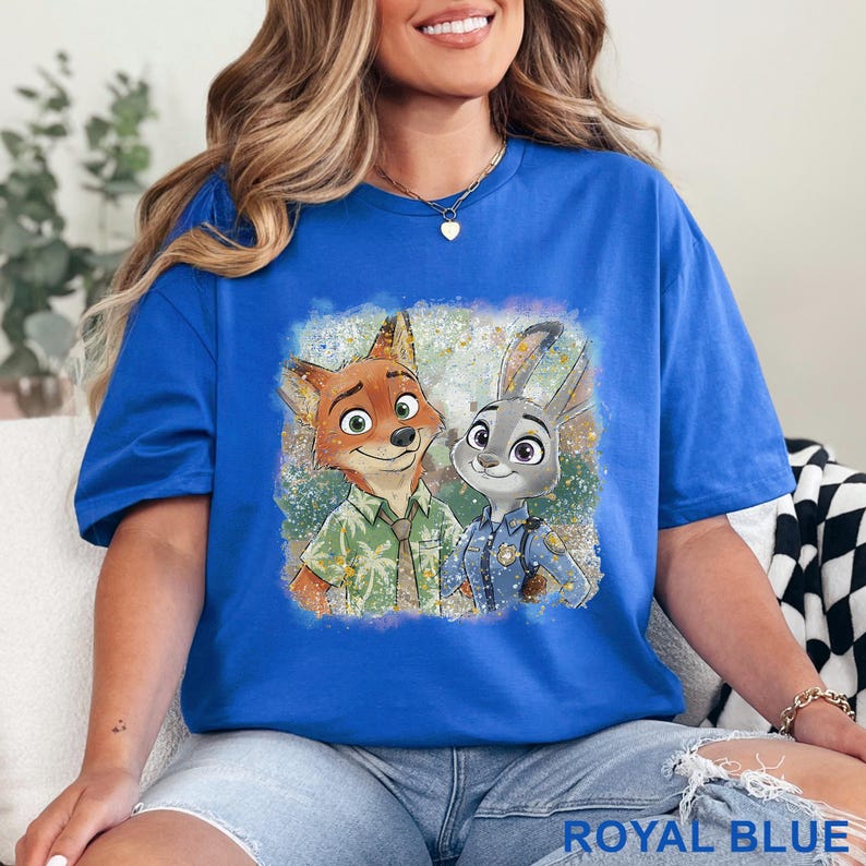 K&ouml;nnte beinhalten: K&ouml;nigsblaues T-Shirt mit einer Grafik von Nick Wilde und Judy Hopps aus Zootopia. Das Bild zeigt die Charaktere l&auml;chelnd. Der Text "ROYAL BLUE" befindet sich am unteren Rand des Shirts.