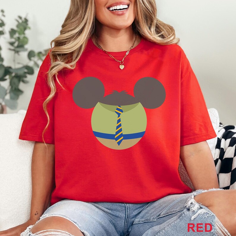 Puede incluir: Camiseta roja con un dise&ntilde;o de personaje de dibujos animados. El dise&ntilde;o incluye orejas marrones, un cuerpo verde y una corbata a rayas azules y amarillas. La palabra "RED" es visible en la esquina inferior derecha.