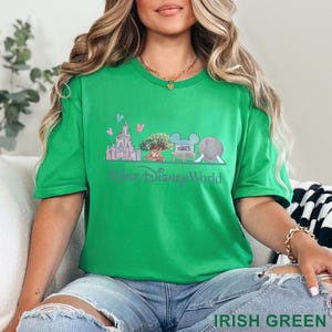 May include: A green t-shirt featuring a Walt Disney World graphic. The design includes a castle, tree, and Spaceship Earth, with the text "Walt Disney World" in a script font. The shirt is labeled "IRISH GREEN".