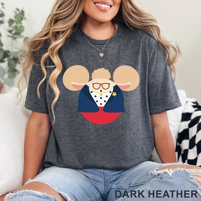 Puede incluir: Camiseta gris oscuro con un dise&ntilde;o de personaje de dibujos animados. El dise&ntilde;o incluye un personaje con gafas, una chaqueta azul y un broche de flor amarilla. El texto "DARK HEATHER" est&aacute; en la parte inferior de la imagen.