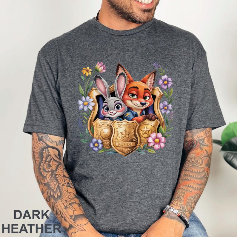 Puede incluir: Camiseta gris jaspeado oscuro con un gr&aacute;fico colorido de Judy Hopps y Nick Wilde de Zootopia, enmarcado por flores y placas de polic&iacute;a. El texto "Zootopia Police" es visible en la placa. La camiseta es de material suave.