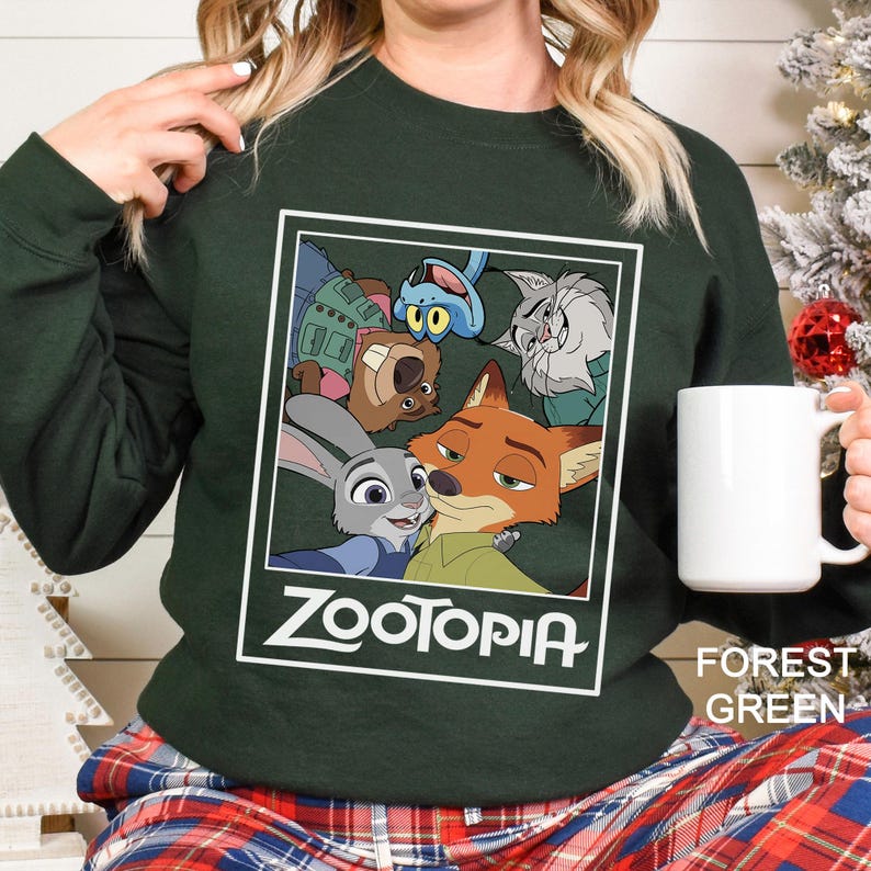 Peut inclure: Sweat-shirt vert for&ecirc;t avec un motif Zootopia. Le motif comprend Judy Hopps, Nick Wilde et d'autres personnages du film d'animation. Le mot "Zootopia" est imprim&eacute; en blanc. Une tasse blanche est tenue dans la main.