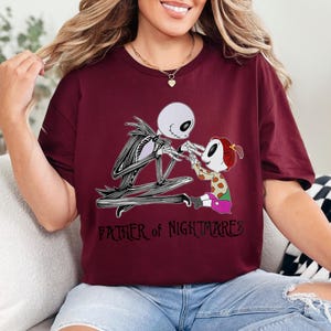 Puede incluir: Camiseta burdeos con un dise&ntilde;o de Jack Skellington y una figura infantil. El texto "FATHER OF NIGHTMARES" est&aacute; impreso debajo. Las figuras son en blanco y negro. La camiseta es de color rojo oscuro.