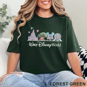 May include: Forest green t-shirt featuring a Walt Disney World graphic. The design includes Cinderella's castle, the Tree of Life, a Mickey Mouse head, and Spaceship Earth. The words "Walt Disney World" are written in a script font.