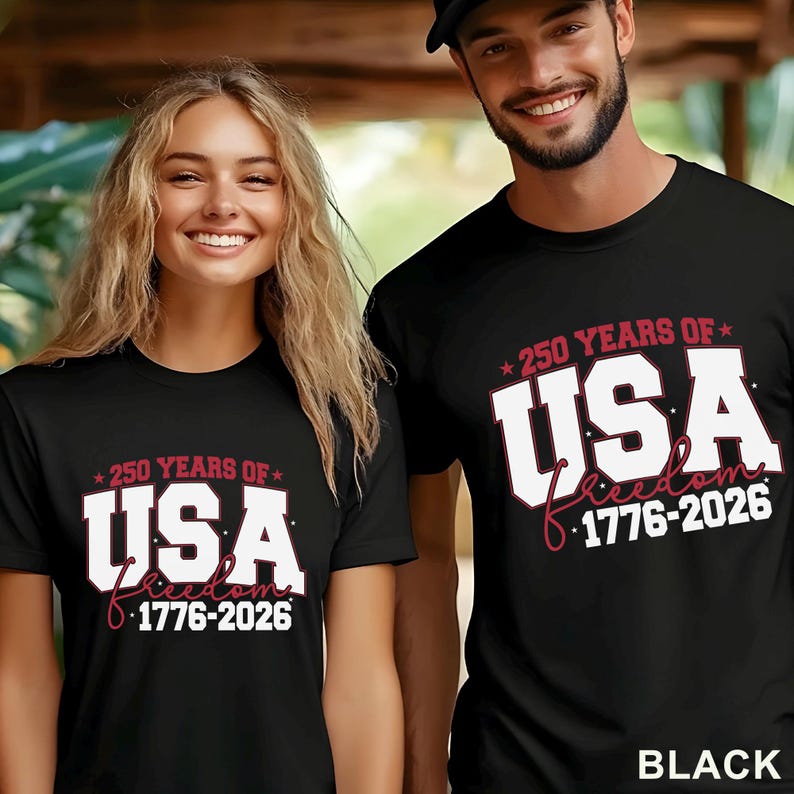 May include: Black t-shirts with the text "250 YEARS OF USA 1776-2026" in white and red. The shirts are worn by two people. The word "Freedom" is written in cursive. The word "BLACK" is written in the bottom right corner.