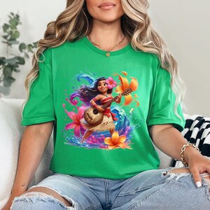 May include: A green t-shirt featuring a vibrant illustration of a cartoon character playing a ukulele. The character is adorned with flowers and surrounded by colorful water and floral elements. The shirt is a solid green color.