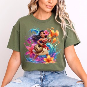 May include: Olive green t-shirt featuring a vibrant graphic of a cartoon character playing a ukulele. The character is surrounded by colorful flowers and water splashes. The design includes a pink flower in the character's hair.