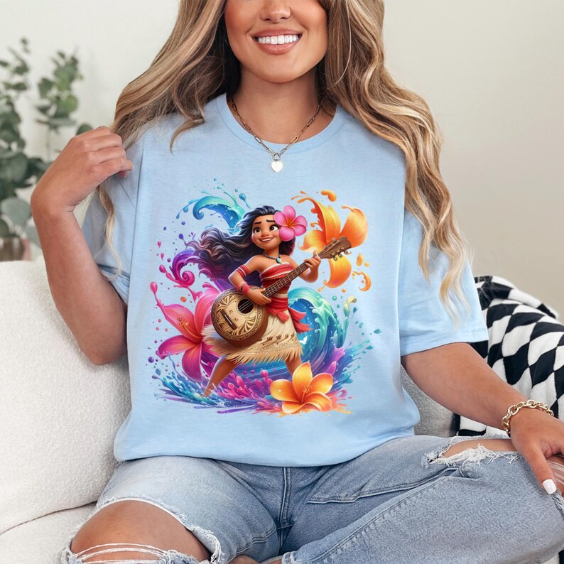 May include: Light blue t-shirt featuring a colorful illustration of a cartoon character playing a ukulele. The character is surrounded by flowers and water splashes. The shirt is made of a soft material.