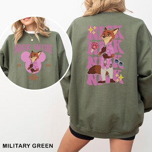 May include: Military green sweatshirt featuring a cartoon fox character in a pink shirt and sunglasses. The front has a pink Mickey Mouse-shaped design with text. The back has the fox graphic and the name "Nick" repeated in pink.