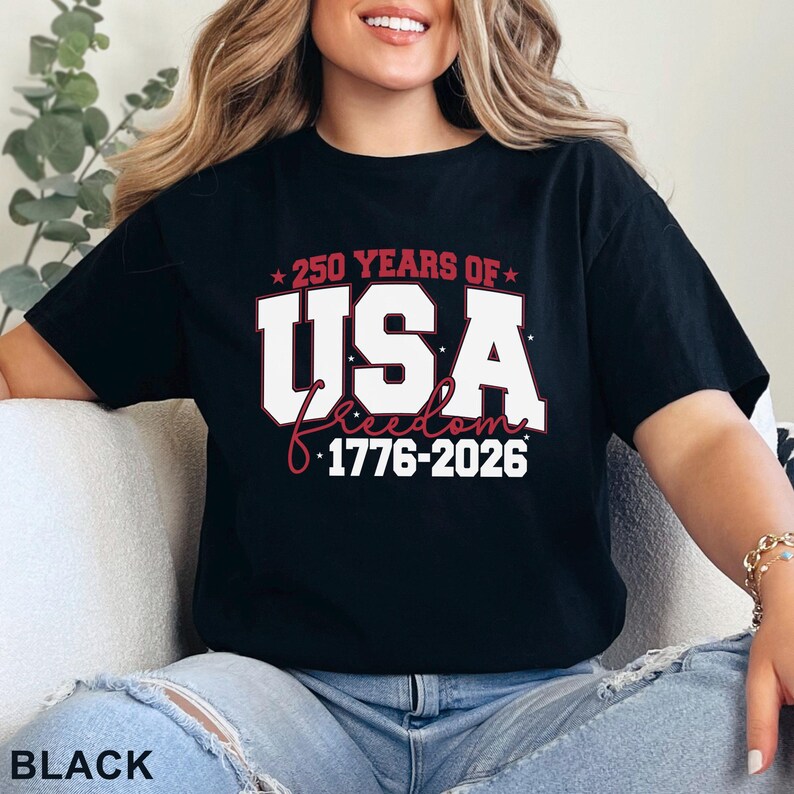 May include: Black t-shirt with the text "250 YEARS OF USA Freedom 1776-2026" in white and red. The shirt has a crew neck and short sleeves. The word "BLACK" is at the bottom of the image.