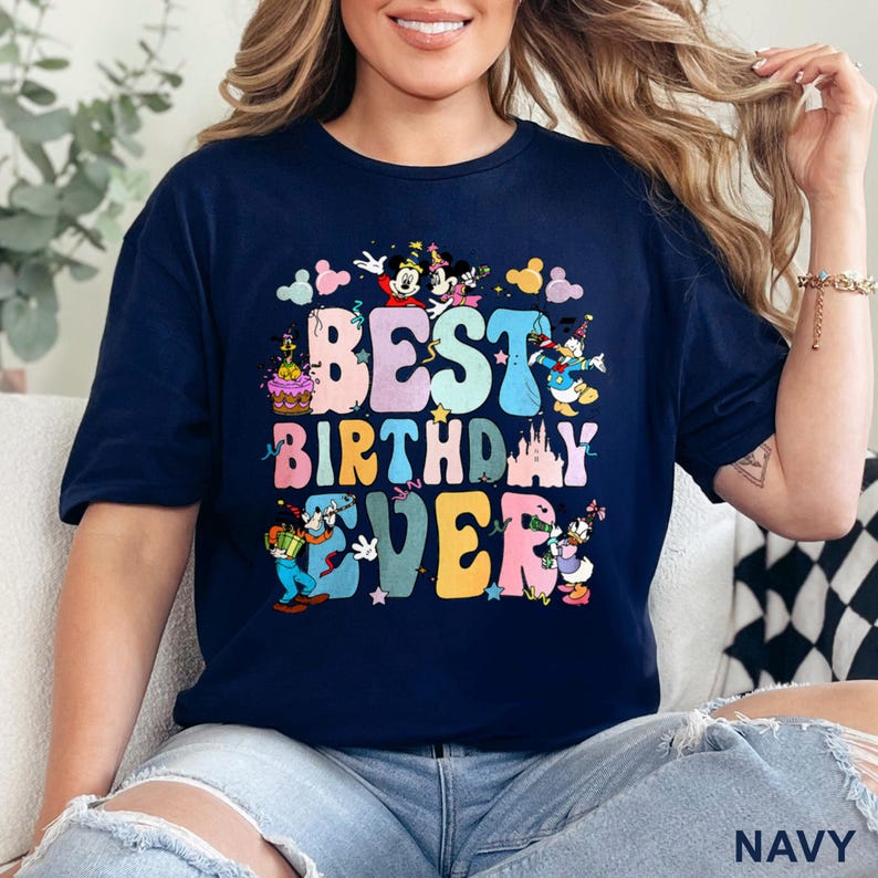 May include: Navy blue t-shirt with the text "BEST BIRTHDAY EVER" in colorful bubble letters. The design includes cartoon characters like Mickey and Minnie Mouse, Donald Duck, and Goofy, with stars and a castle.