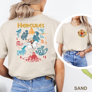 May include: Sand-colored t-shirt featuring a colorful graphic of Hercules and various mythological creatures. The back of the shirt displays the word "Hercules" in gold lettering above the graphic. A smaller graphic of Hercules is on the front.