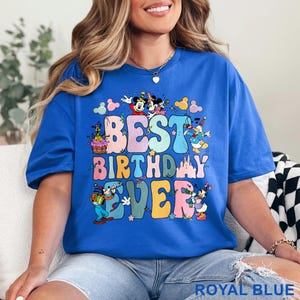 May include: Royal blue t-shirt with the text "BEST BIRTHDAY EVER" in colorful bubble letters. The design includes cartoon characters like Mickey and Minnie Mouse, Donald Duck, and Goofy, with a birthday cake and balloons.