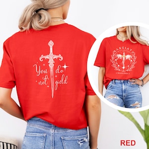 May include: Red t-shirts with white graphic designs. One shirt features a sword with the text "You do not yield." The other shirt has a circular design with text that reads "Basgiath War College" and "Dragon Rider".