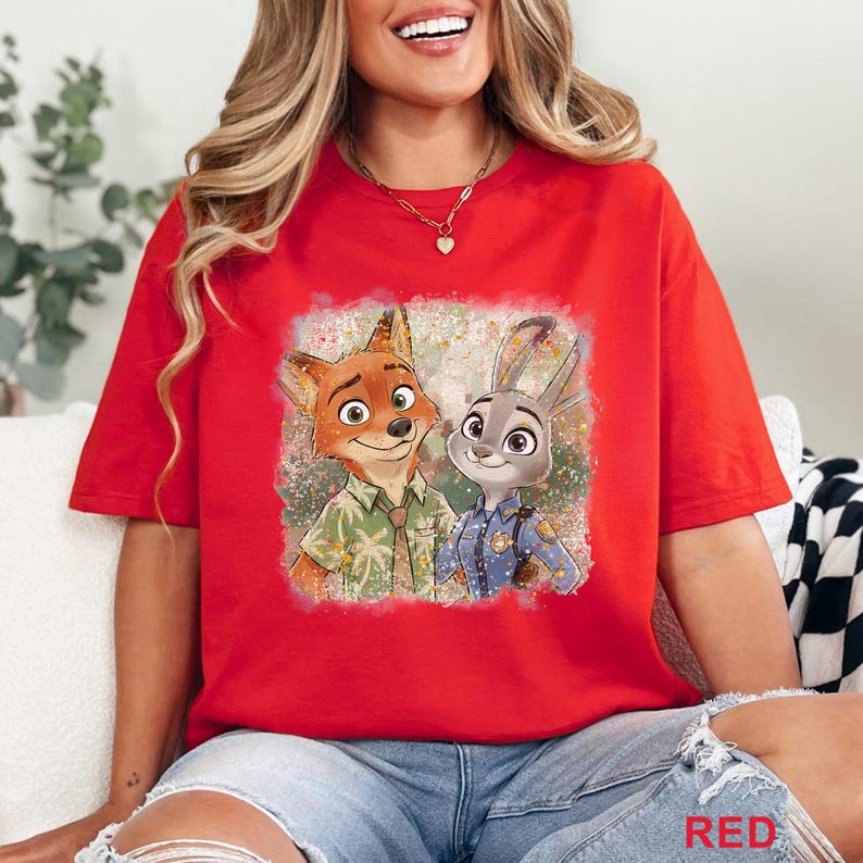 K&ouml;nnte beinhalten: Rotes T-Shirt mit einem farbenfrohen Aufdruck von Nick Wilde und Judy Hopps aus dem Animationsfilm Zootopia. Die Charaktere sind in einer freundlichen Pose dargestellt, Nick tr&auml;gt ein Hawaiihemd und Judy eine Polizeiuniform.