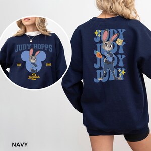 May include: Navy blue sweatshirt featuring Judy Hopps from Zootopia. The front design includes the text "JUDY HOPPS" and a cartoon image of Judy. The back displays Judy with a carrot and the text "JUDY".