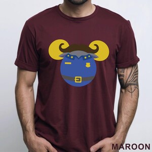 Puede incluir: Camiseta granate con un dise&ntilde;o de carnero de dibujos animados con uniforme de polic&iacute;a. El carnero tiene cuernos amarillos, bigote marr&oacute;n y uniforme azul con estrellas doradas y una placa. La palabra "MAROON" est&aacute; impresa en la parte inferior.