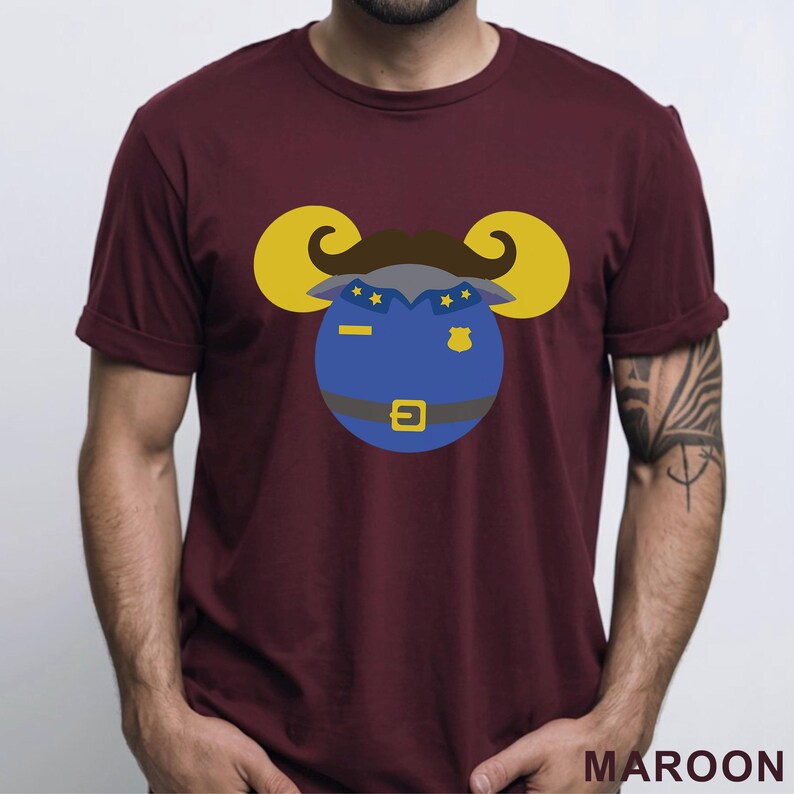 Puede incluir: Camiseta granate con un dise&ntilde;o de carnero de dibujos animados con uniforme de polic&iacute;a. El carnero tiene cuernos amarillos, bigote marr&oacute;n y uniforme azul con estrellas doradas y una placa. La palabra "MAROON" est&aacute; impresa en la parte inferior.
