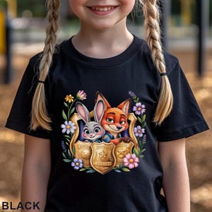 Puede incluir: Camiseta negra con un gr&aacute;fico colorido de Judy Hopps y Nick Wilde de Zootopia dentro de una placa de polic&iacute;a, rodeada de flores. La palabra "BLACK" est&aacute; impresa en la parte inferior de la camiseta.
