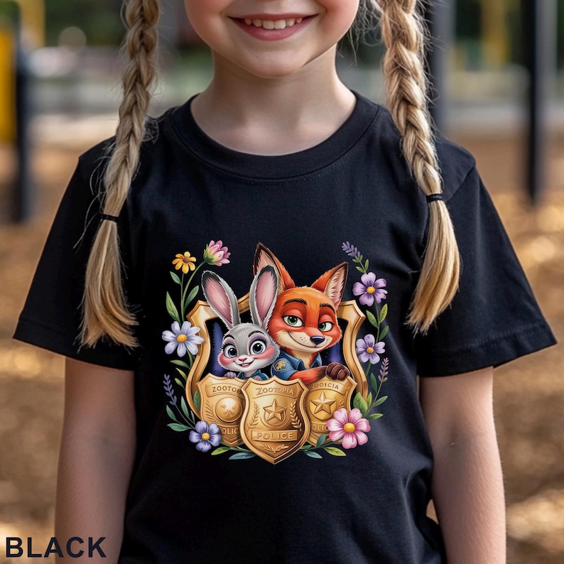 Puede incluir: Camiseta negra con un gr&aacute;fico colorido de Judy Hopps y Nick Wilde de Zootopia dentro de una placa de polic&iacute;a, rodeada de flores. La palabra "BLACK" est&aacute; impresa en la parte inferior de la camiseta.