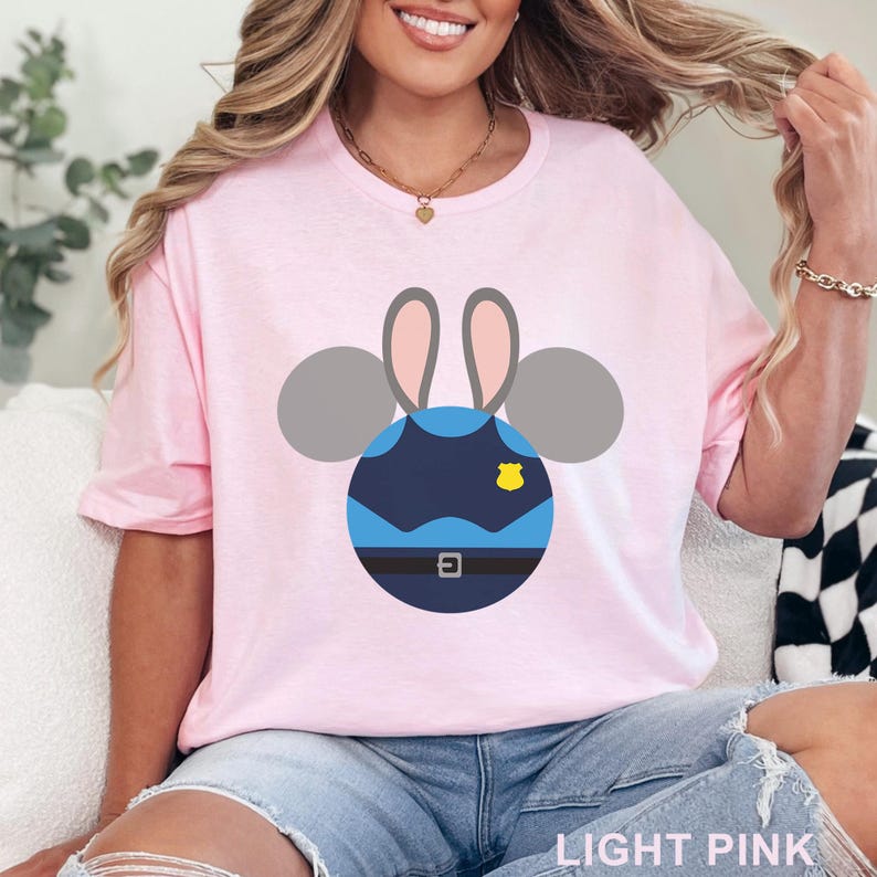 Puede incluir: Camiseta rosa claro con un dise&ntilde;o de dibujos animados de un uniforme de polic&iacute;a con orejas de rat&oacute;n. El dise&ntilde;o es azul, gris y amarillo. El texto "LIGHT PINK" est&aacute; en la parte inferior de la camiseta.
