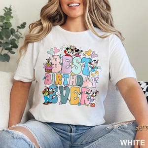 May include: White t-shirt with the text "BEST BIRTHDAY EVER" in colorful bubble letters. The design includes cartoon characters like Mickey and Minnie Mouse, Donald Duck, and Goofy, with balloons and a castle.