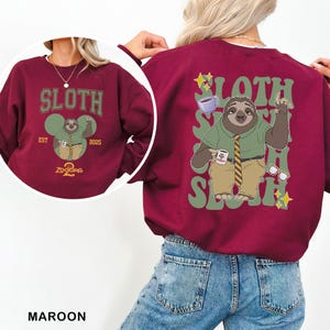May include: Maroon sweatshirt featuring a cartoon sloth character from Zootopia. The front design includes the word "SLOTH" and the text "EST 2025". The back design shows the sloth with the word "SLOTH" repeated vertically. The sloth is wearing a green shirt and a tie.