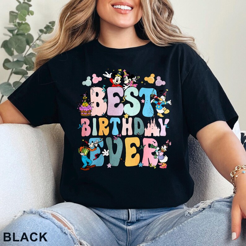May include: Black t-shirt with the text "BEST BIRTHDAY EVER" in colorful bubble letters. The design includes cartoon characters like Mickey Mouse, Minnie Mouse, Donald Duck, and Goofy. The shirt is a casual, unisex style.