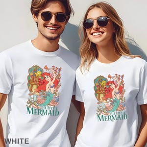 May include: White t-shirts featuring a colorful graphic of Ariel from The Little Mermaid, with the text "THE LITTLE MERMAID" in green. The design includes Ariel, Flounder, and Sebastian, surrounded by floral elements. The word "WHITE" is at the bottom.