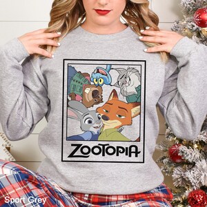 Peut inclure: Sweat-shirt gris Sport avec un col rond et des manches longues. Le devant pr&eacute;sente un graphisme encadr&eacute; des personnages du film d'animation Zootopia, dont Judy Hopps et Nick Wilde. Le mot "Zootopia" est imprim&eacute; en noir.