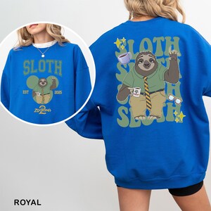 May include: Royal blue sweatshirt featuring a cartoon sloth character from Zootopia. The front design includes the word "SLOTH" above an image of the sloth holding a coffee cup. The back design repeats "SLOTH" with the sloth character, coffee cup, and glasses.