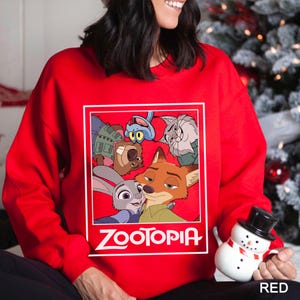 Peut inclure: Un sweat-shirt rouge avec un motif des personnages du film d'animation "Zootopie" dans un cadre rectangulaire blanc. Le mot "Zootopia" est imprim&eacute; en blanc en dessous. Le sweat-shirt est de couleur rouge uni.
