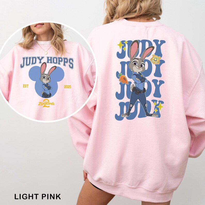May include: Light pink sweatshirt featuring Judy Hopps from Zootopia. The front design includes the text "JUDY HOPPS" above a cartoon image of Judy. The back features a larger Judy Hopps graphic with the word "JUDY" repeated.
