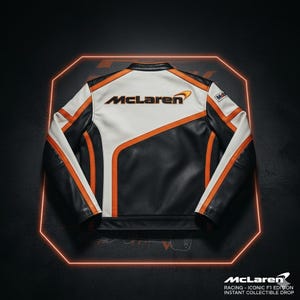 Puede incluir: Chaqueta de cuero negra, blanca y naranja con el logotipo de McLaren en la espalda. La chaqueta tiene un dise&ntilde;o de carreras cl&aacute;sico con rayas y detalles en naranja. El logotipo de McLaren tambi&eacute;n se muestra en la parte inferior de la imagen.