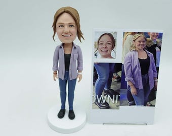 May include: A custom bobblehead figurine of a person wearing a purple button-down shirt, black top, and blue jeans. The figurine is on a white base. A photo collage of the person is displayed next to the figurine.