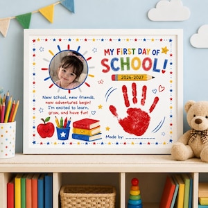 Pode incluir: Um quadro personalizado intitulado My First Day of School com um espaço circular para fotos, uma impressão de mão vermelha, um lápis amarelo com a etiqueta 2026-2027, uma maçã vermelha, um porta-lápis azul e três livros coloridos no fundo branco.