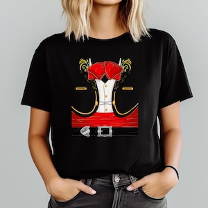May include: Black t-shirt featuring a graphic of a mariachi outfit. The design includes a red bow tie, a white shirt, a black jacket with gold trim, and a red belt with a silver buckle. The graphic is centered on the shirt.