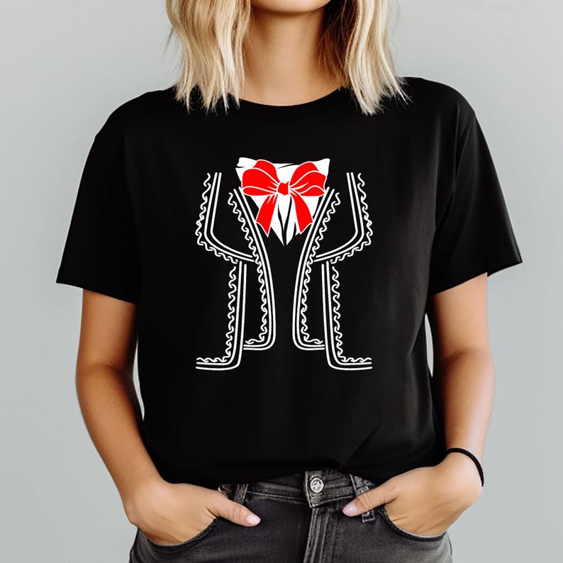 May include: Black t-shirt featuring a graphic of a mariachi suit. The design includes a white shirt, a red bow tie, and a black jacket with white trim. The shirt is a crew neck style.