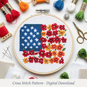 May include: A cross-stitch pattern of the American flag, featuring a blue field with white stars and red and yellow flowers. The design is set in a wooden embroidery hoop, surrounded by spools of thread, needles, and scissors. The text "Cross Stitch Pattern - Digital Download" is at the bottom.