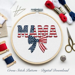 Pode incluir: Um bastidor de bordado com a palavra "MAMA" em vermelho, branco e azul, assemelhando-se à bandeira americana. Uma fita com um desenho estrelado e listras vermelhas está abaixo da palavra. Fios de bordar, agulhas e tesouras circundam o bastidor.