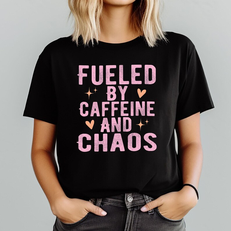 May include: Black t-shirt with the text "FUELED BY CAFFEINE AND CHAOS" in pink, with star and heart graphics. The shirt is a crew neck and is being worn.