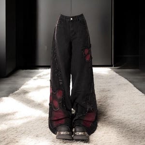 Könnte beinhalten: Schwarze, weite Jeans mit Destroyed-Details und roten Schmetterlings-Applikationen. Die Jeans sind auf einem weißen Teppich abgebildet.