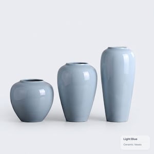 Könnte beinhalten: Drei hellblaue Keramikvasen in unterschiedlichen Höhen und Formen. Das Set besteht aus einer kurzen, bauchigen Vase, einer mittelgroßen, konischen Vase und einer hohen, schlanken Vase. Jedes Stück hat eine glatte, glänzende Oberfläche.