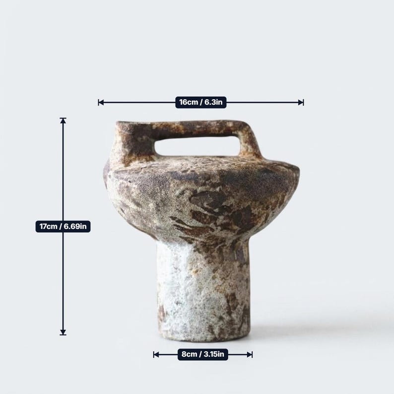 May include: A textured brown and grey ceramic vessel with a handle, measuring 6.3 inches in width, 6.69 inches in height, and 3.15 inches at the base. The object features a mottled, weathered surface finish with a cylindrical base and wide top.